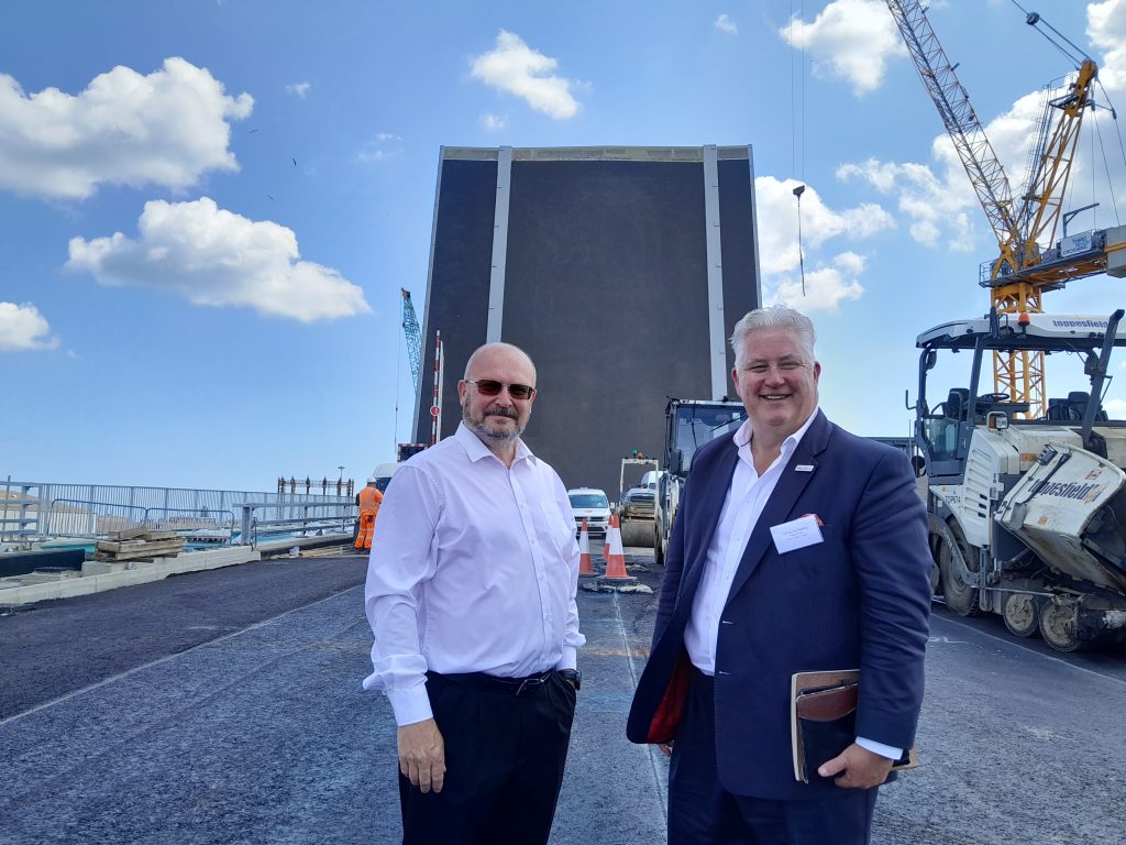 Councillor Graham Plant and Councillor Kevin Bentley standing in front of a raised bridge during construction.