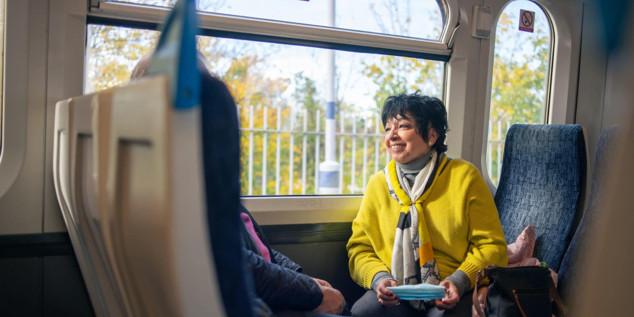 Smiling woman wearing yellow coat and sitting on a train