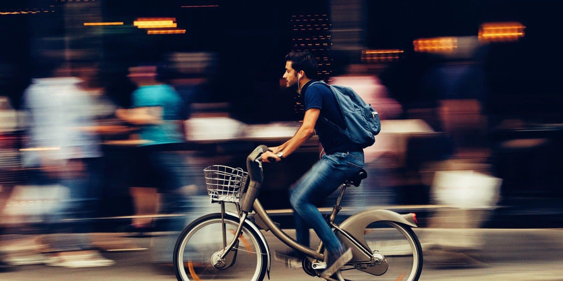Man riding a bike through a city. The background is blurred.