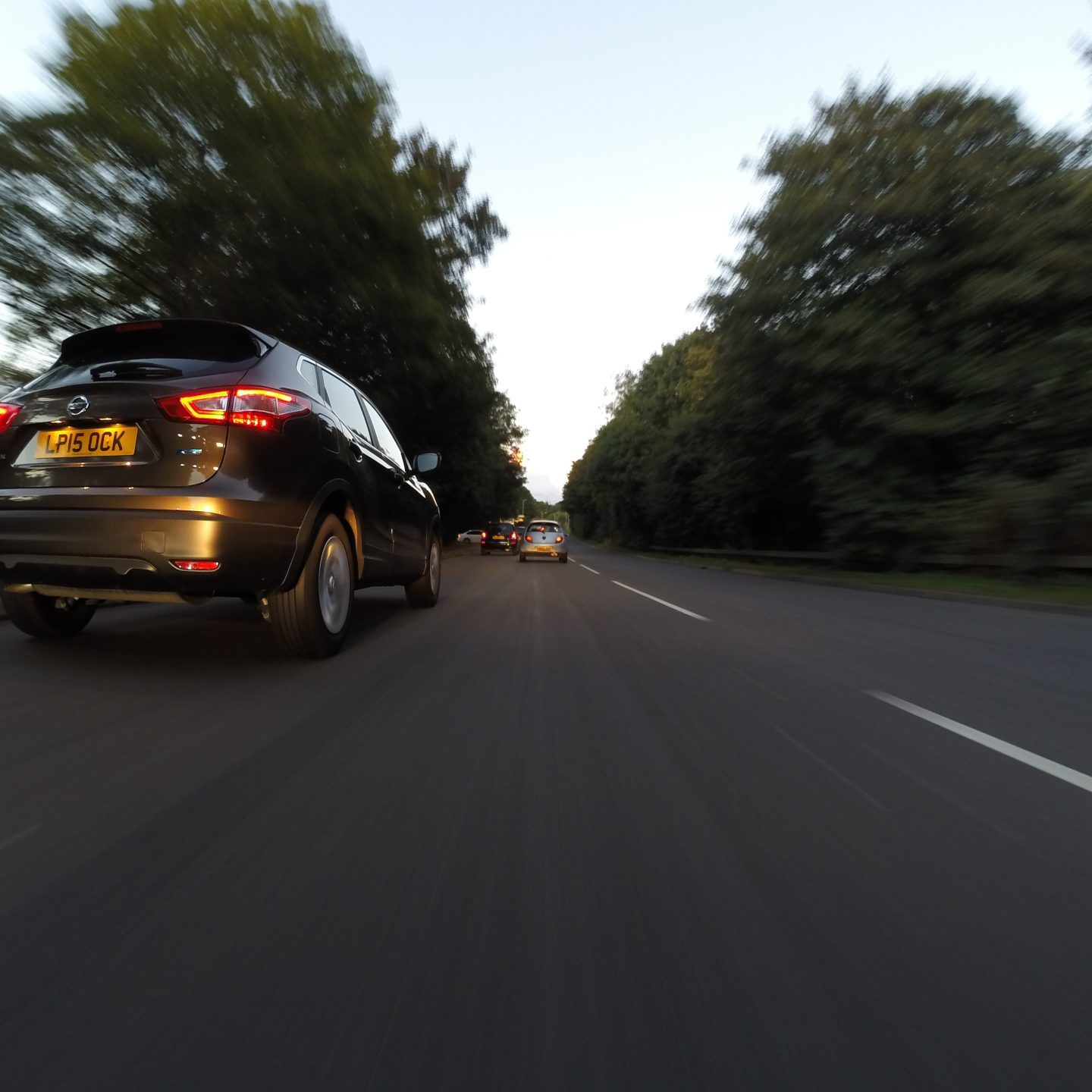 Black car driving behind others cars on a road with a blurred background.
